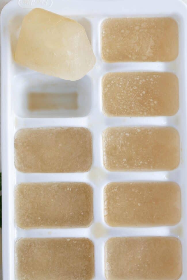 A white ice cube tray filled with frozen chicken broth ice cubes