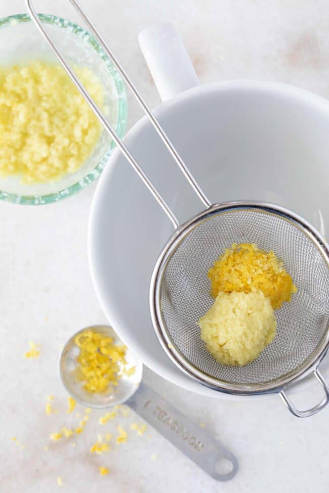 A metal strainer with grated lemon zest sits in a white cup.