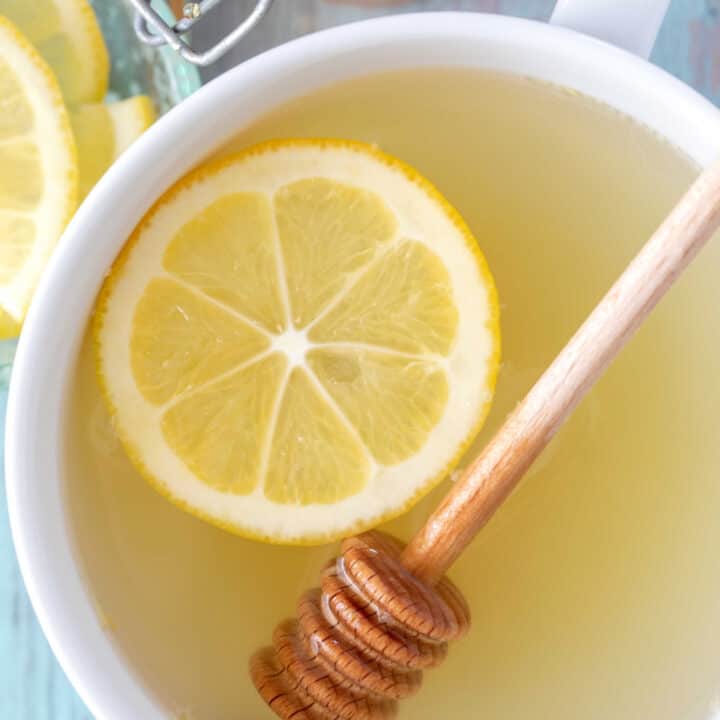 A white cup filled with lemon ginger tea and a lemon slice.