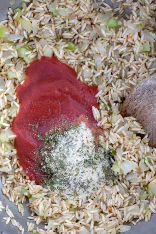 A pot filled with long grain brown rice, tomato paste and seasoning. 