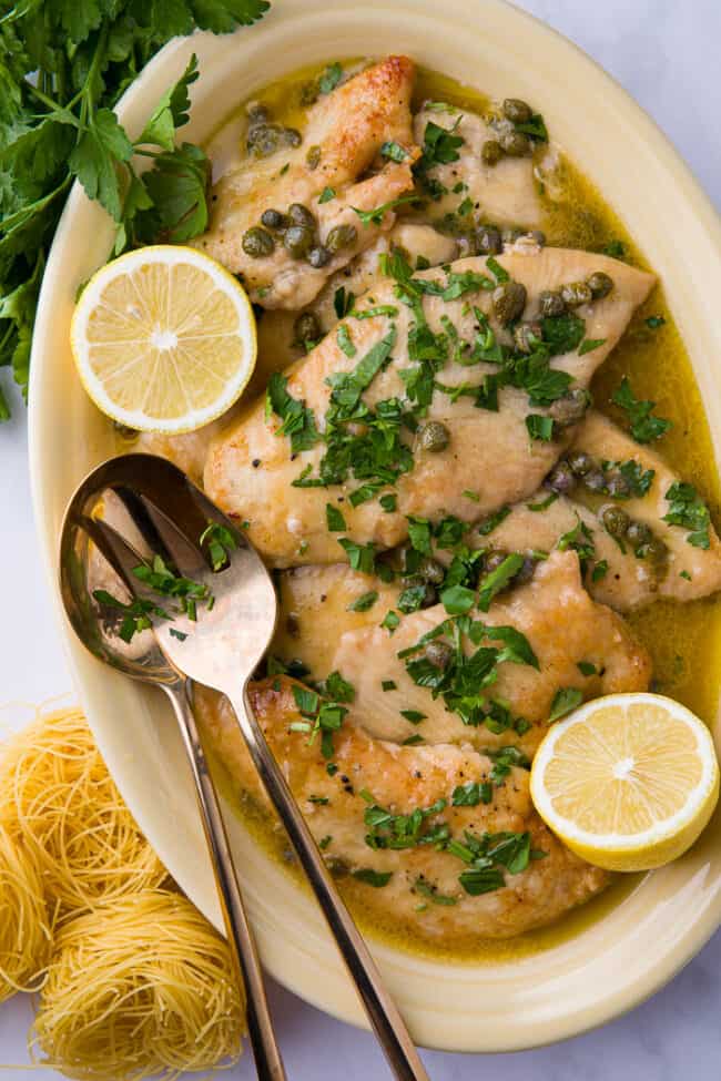 A yellow platter of lemon chicken piccata.