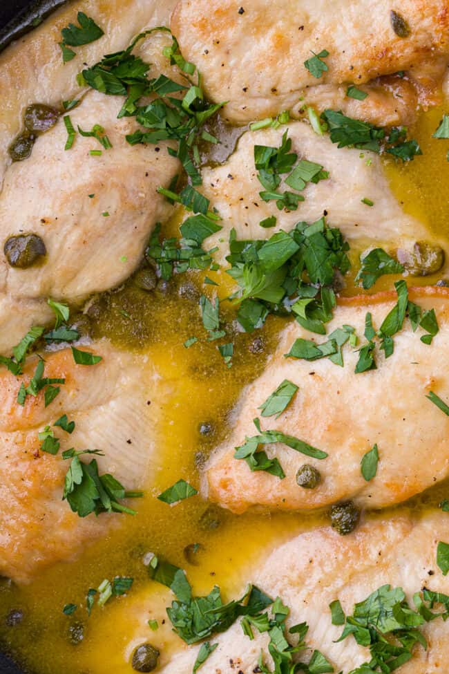 A black skillet filled with chicken piccata sprinkled with chopped parsley and capers.