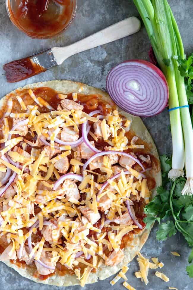 A flour tortilla covered with bbq sauce, chopped cooked chicken and cheese.