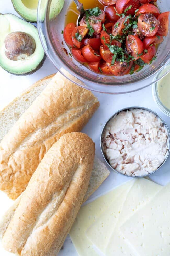 baguette, can of tuna, cheese slices and bowl of tomatoes