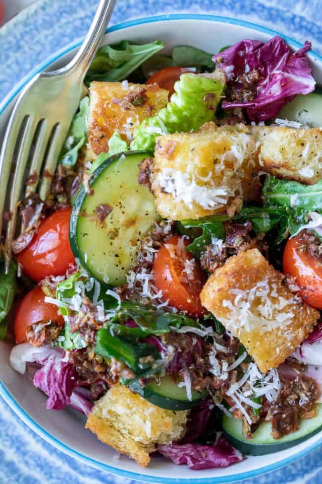 A bowl of salad showing a close up of Greek salad dressing drizzled over the lettuce and cucumber.