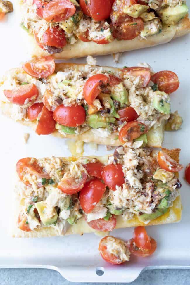 A silvered colored tray filled with marinated cherry tomatoes and avocado on baguette slices.