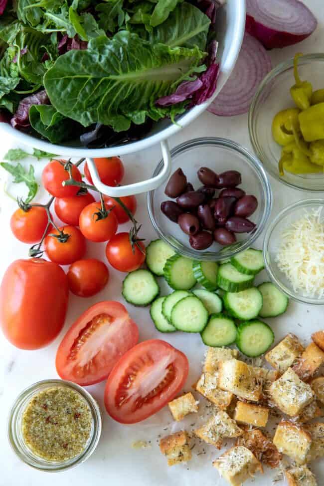 Salad ingredients (lettuce, tomatoes, cucumber, pepperoncini and kalamata olives) for recipe for Italian salad.