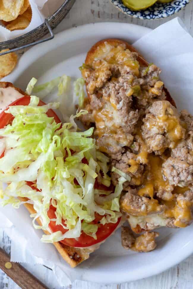 A white plate with a chopped cheese sandwich on a French roll.