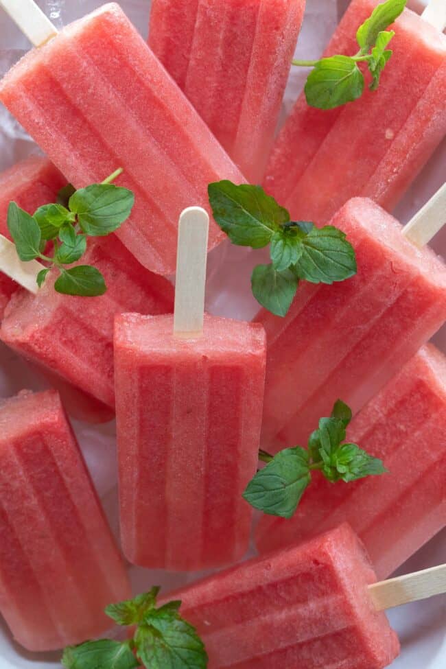 Several watermelon popsicles placed in a bowl with ice.