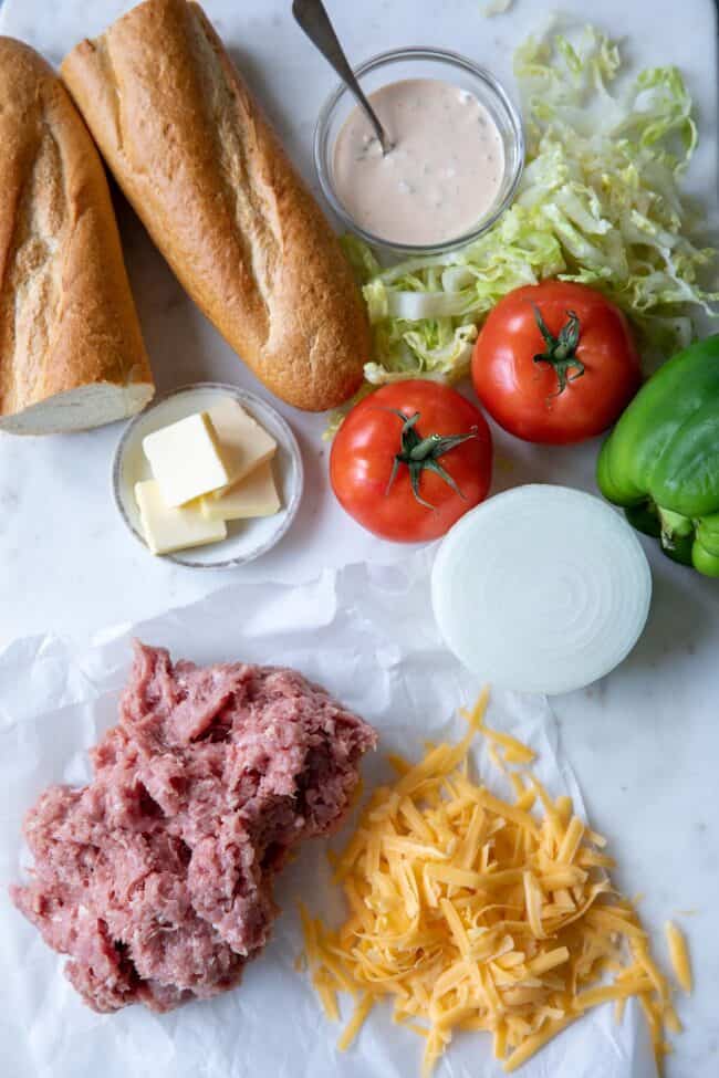 white countertop with hoagie rolls, tomatoes, grated cheese and ground turkey to make a sandwich
