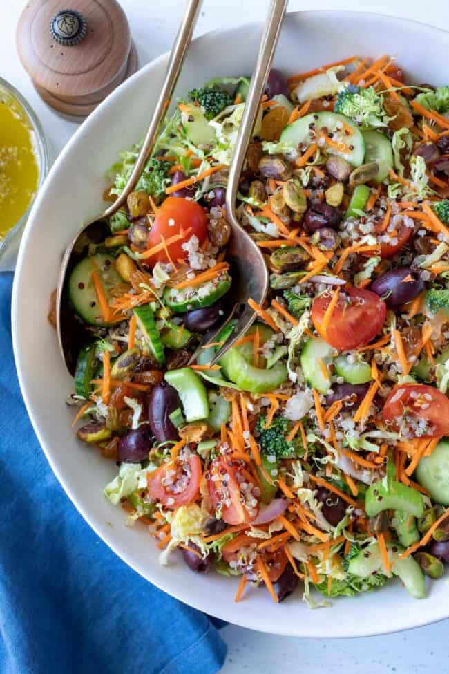 A white bowl filled with the best quinoa salad. Salad servers rest in the bowl.