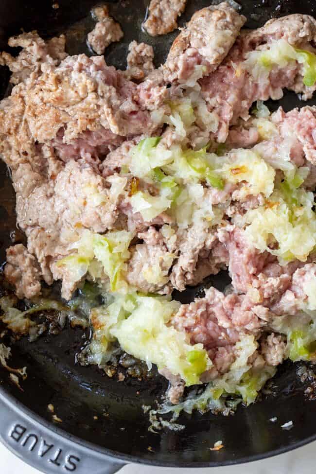 A cast iron skillet cooking ground turkey with grated onion and bell pepper.