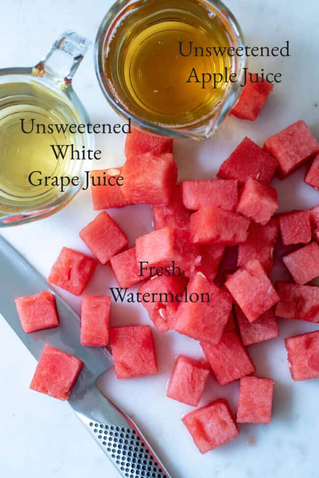 Cubes of chopped watermelon next to a knife on a white countertop. 