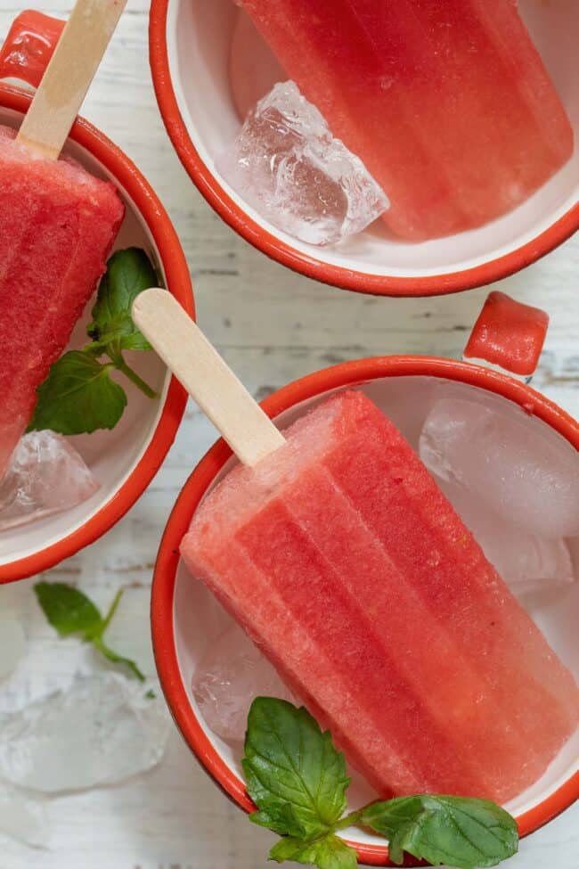 Three frozen fruit pops each in white cup with ice.