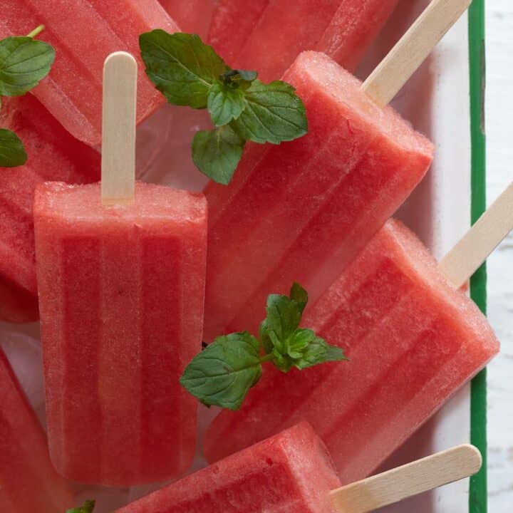 Several watermelon popsicles placed in a white bowl with ice.