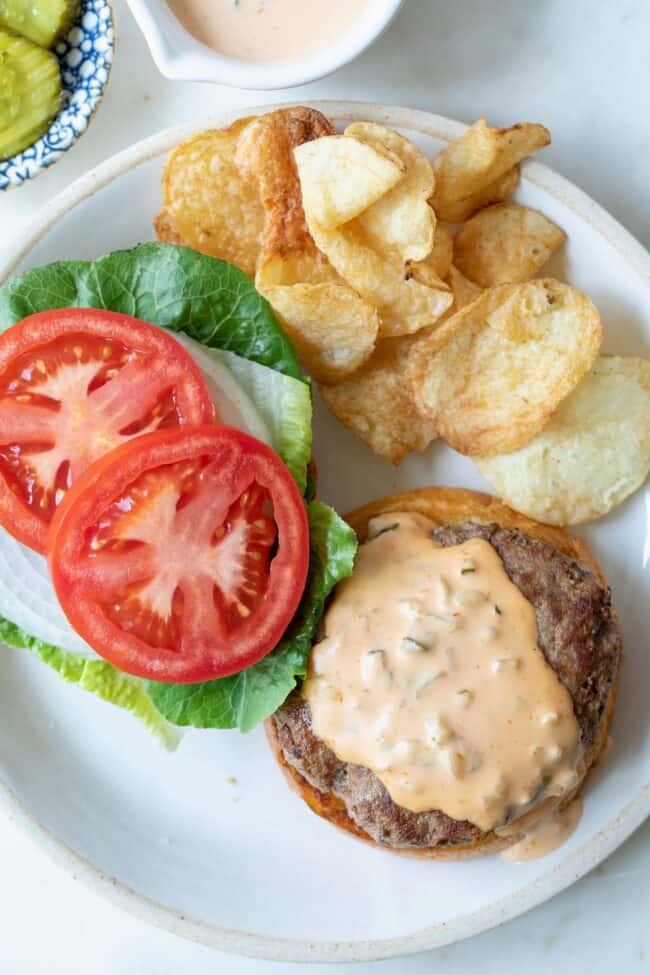 white plate with burger, sliced tomatoes, lettuce and potato chips