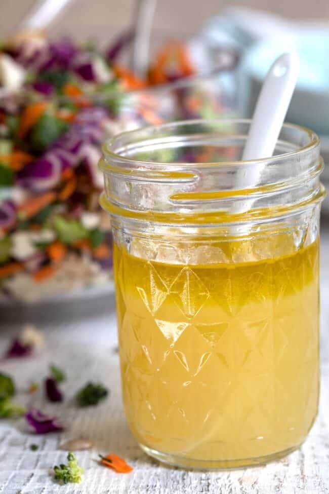 A clear glass mason jar filled with ginger lemon and honey (ginger salad dressing) and a spoon.