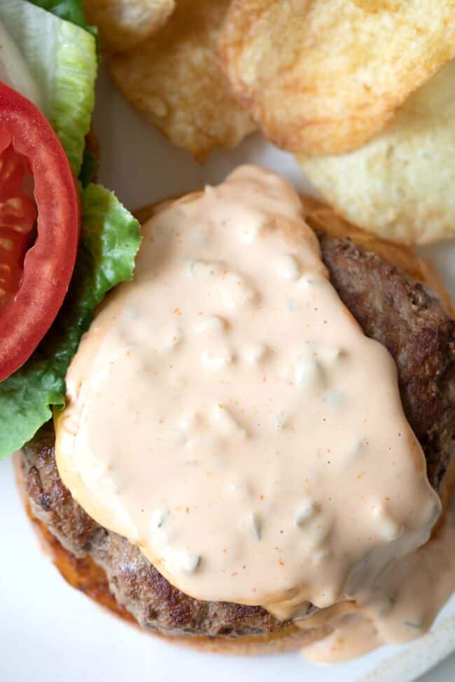 A cooked hamburger with sauce, lettuce and tomato.