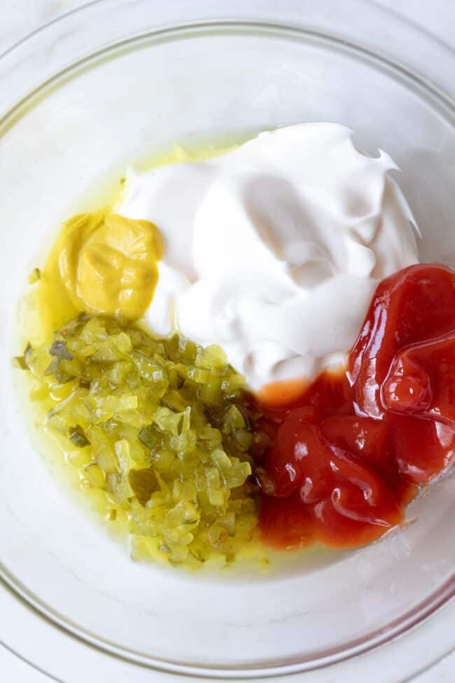 A clear glass bowl with mayonnaise, ketchup, mustard and pickle relish.
