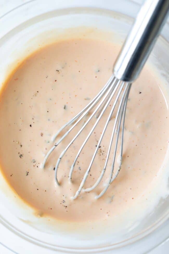 A clear glass bowl with a wire whisk in a creamy burger sauce.