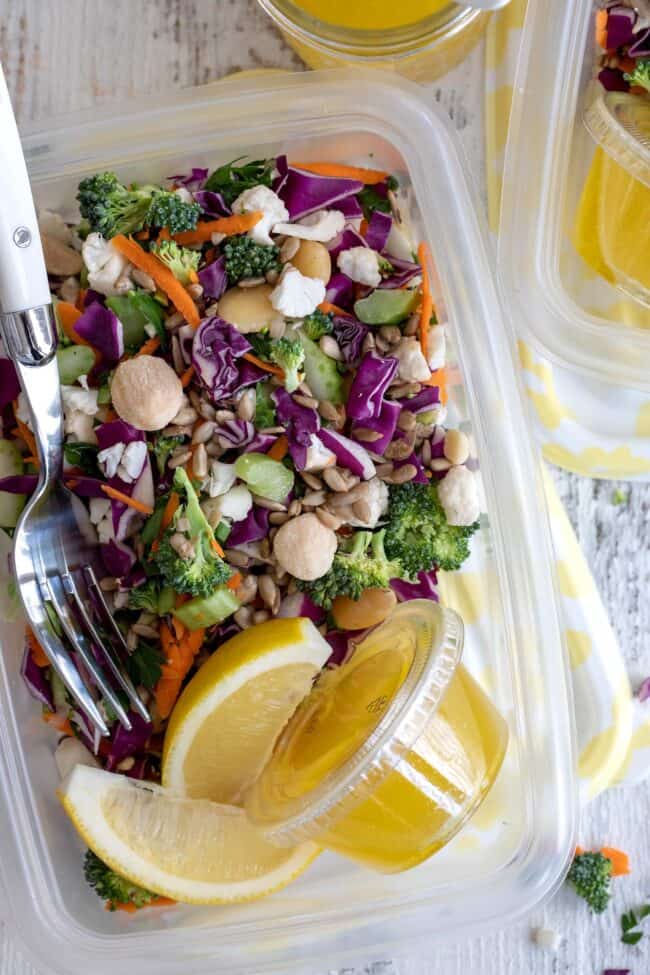 A plastic bowl filled with mixed greens and a plastic container filled with vinaigrette.