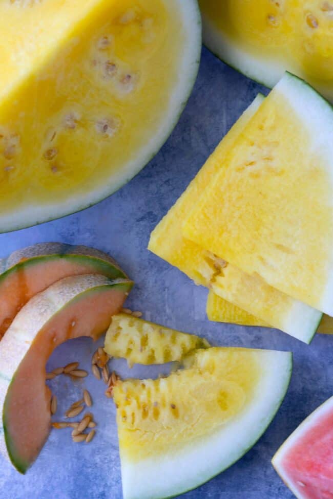 Large cut pieces of yellow watermelon next to slices of cantaloupe and red watermelon