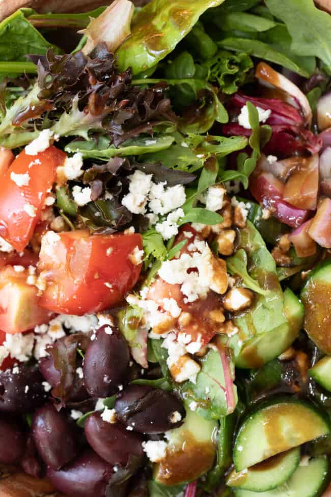 A close up of salad with tomatoes, cucumbers, feta cheese, kalamata olives tossed in balsamic vinaigrette.