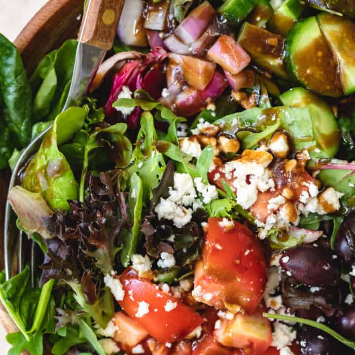 wooden bowl filled with Mediterranean salad and serving spoons