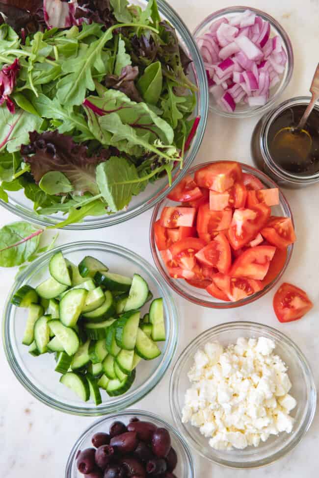 clear glass bowls filled with lettuce and vegetables to make a Mediterranean salad.