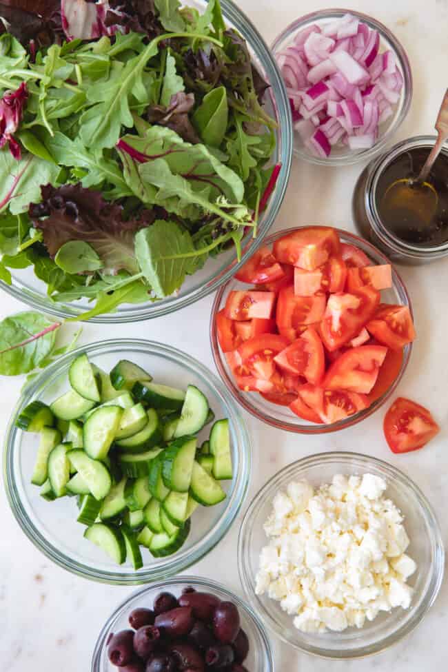 Clear glass bowls filled with lettuce and vegetables to make a Mediterranean salad.