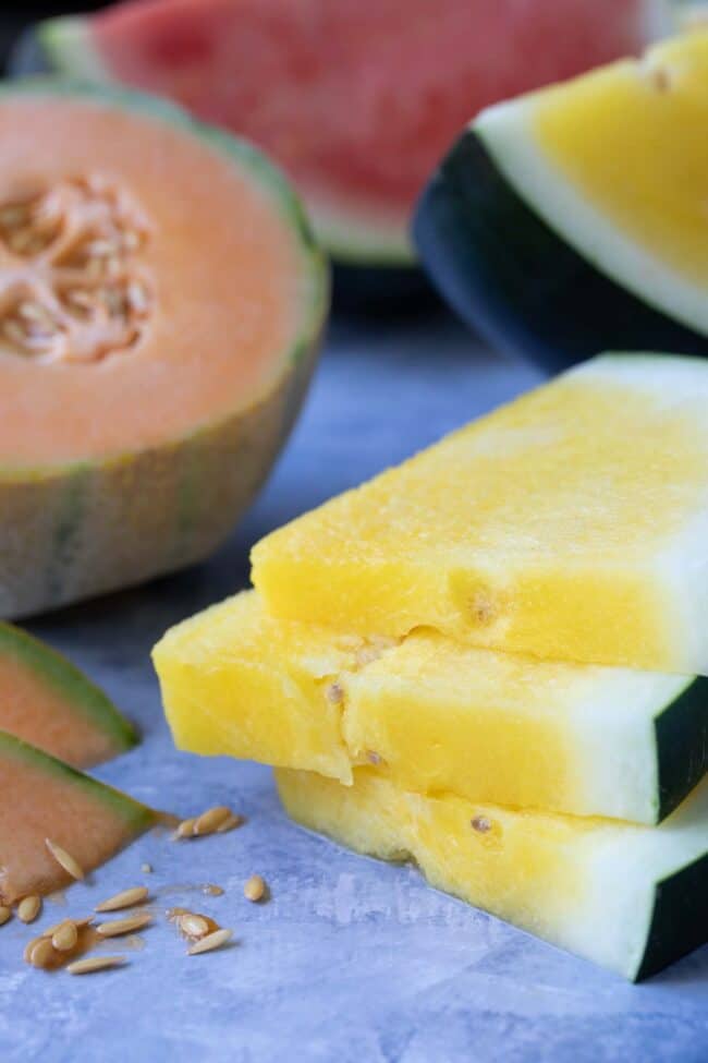 Slices of yellow watermelon stacked next to cantaloupe, red and yellow watermelon
