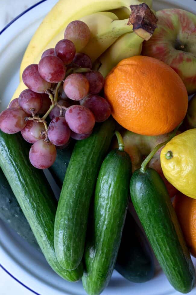 A white bowl filled with apples, bananas, oranges, lemons and grapes