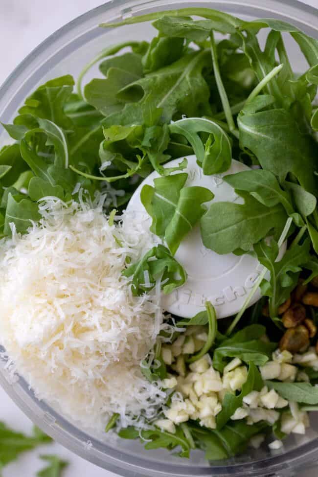 A food processor filled with greens, cheese, garlic and pistachios.