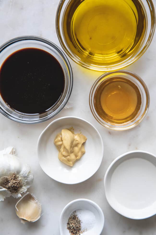 Small glass bowls and white bowls filled with ingredients to make a salad dressing.