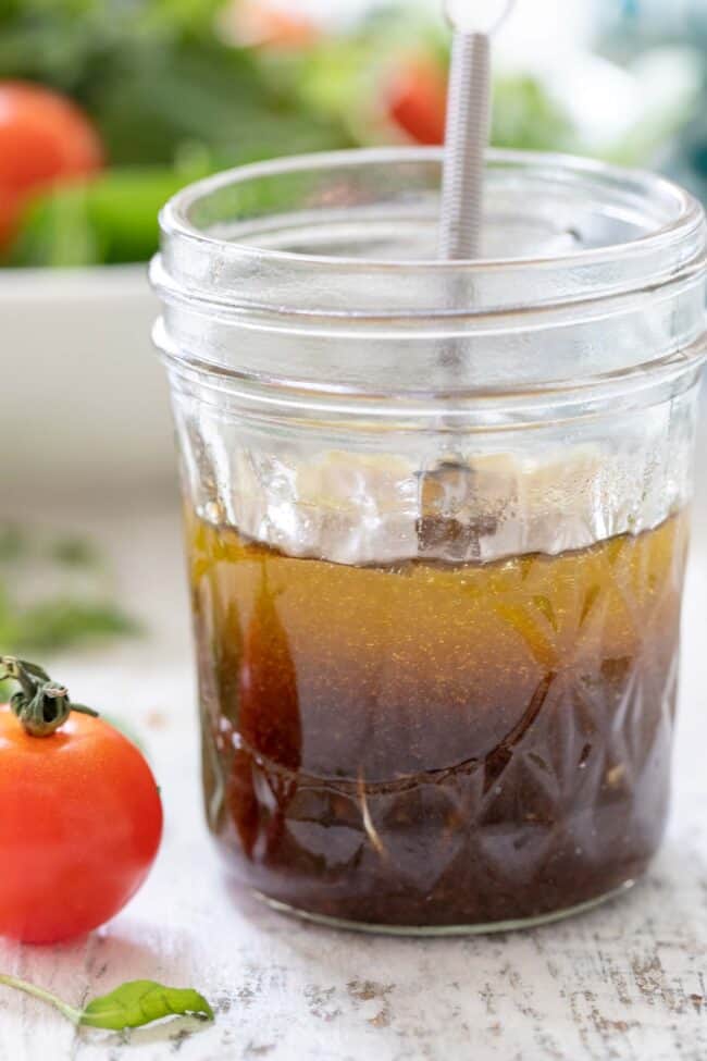 Mason jar filled with balsamic vinegar and olive oil. A whisk is in the jar and a salad is in the background.