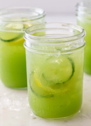 Three clear mason jars filled with cucumber juice and slices of lemon and cucumber