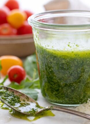 glass jar filled with arugula pesto. A spoon with pesto in it sits next to the jar.