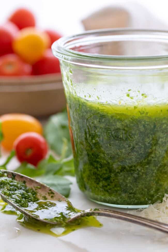 A glass jar filled with green sauce. A spoon with green sauce in it sits next to the jar.
