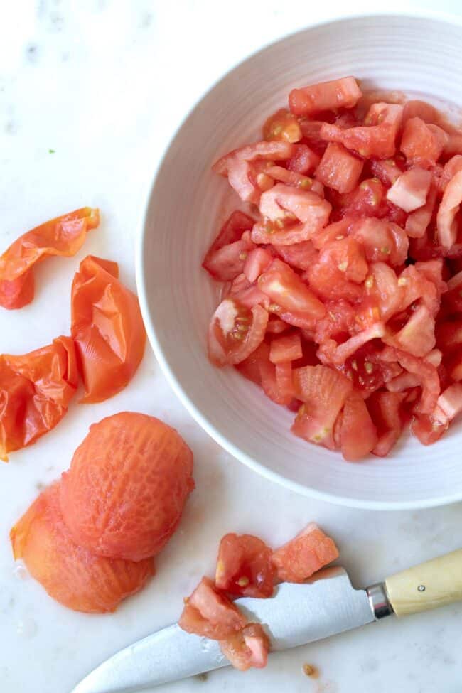 A white bowl filled with peeled and chopped tomatoes. A knife sits next to the bowl.