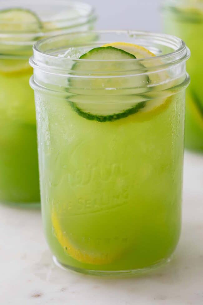 Clear glass mason jar filled with cucumber juice. Slices of cucumber and lemon float in the glass.