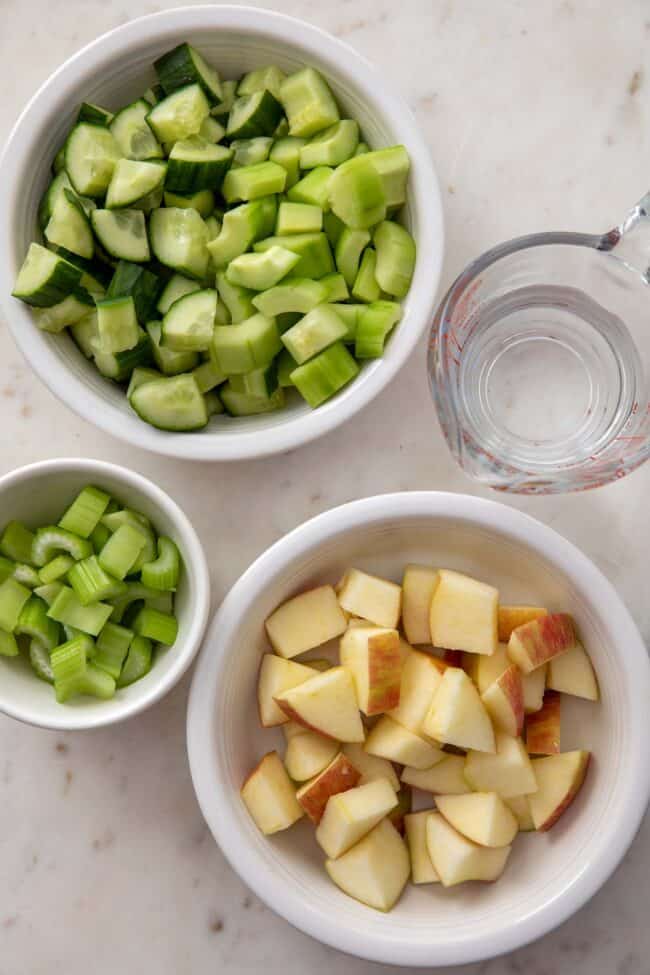 Three white bowls filled with chopped celery and apple.