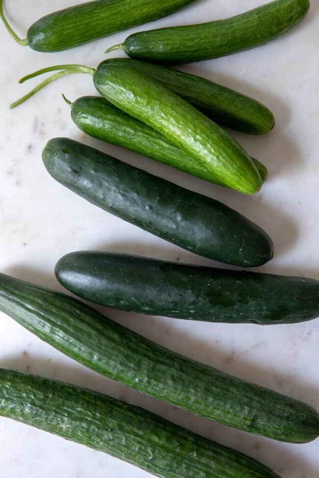 Various types of cucumbers on a white cutting board