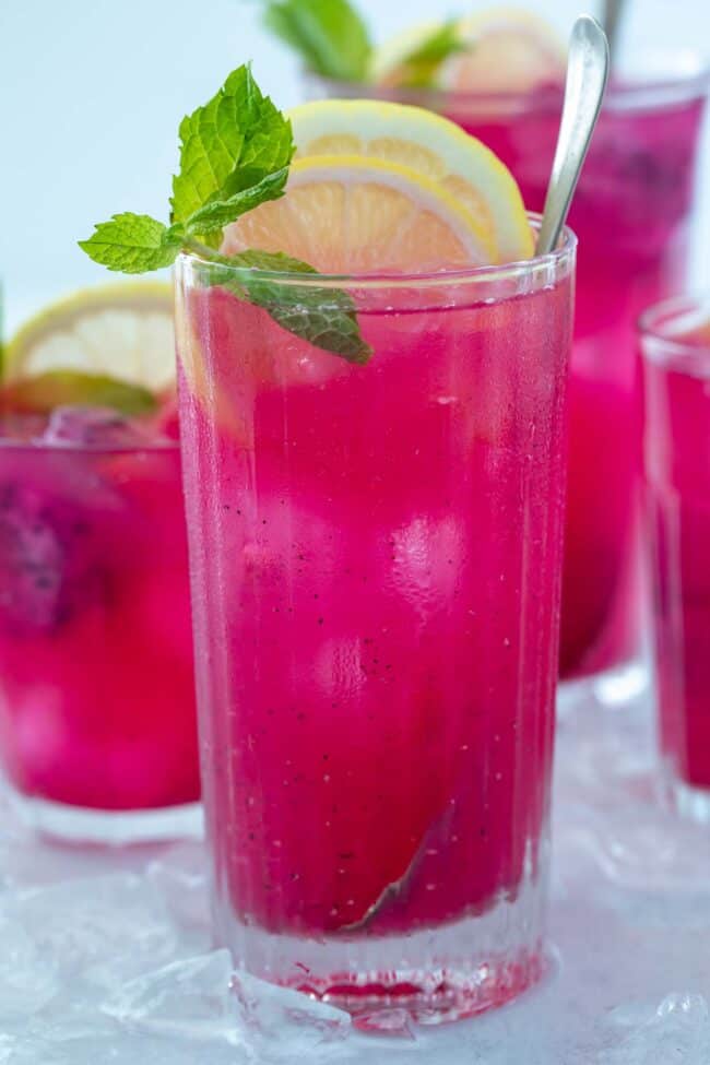 4 glassess filled with bright pink mango dragonfruit refresher. Lemon slices and mint leaves garnish the drinks.