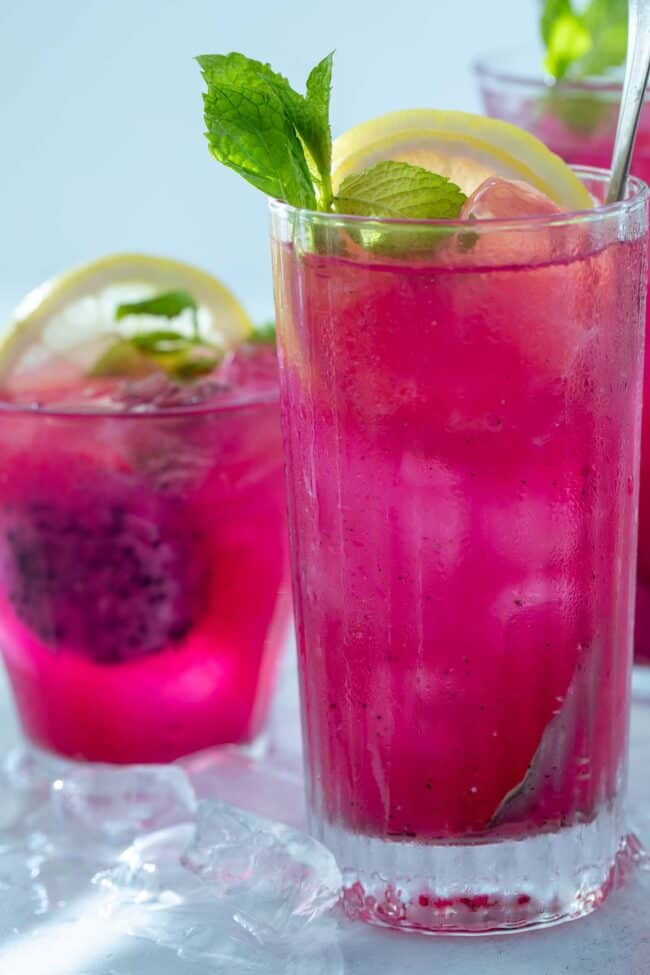 3 glassess filled with bright pink mango dragonfruit refresher. Lemon slices and mint leaves garnish the drinks.