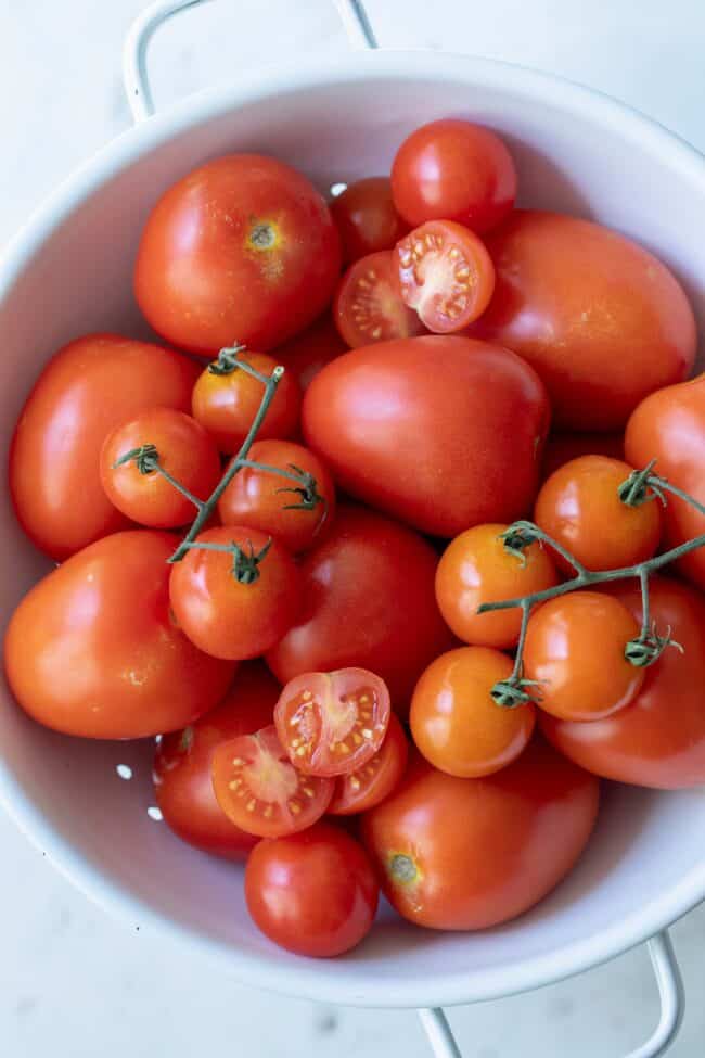 a white colander filled with roma tomatoes and cherry tomatoes