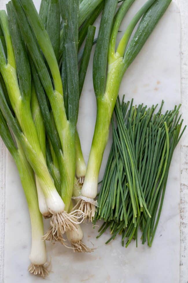 A white cutting board with two a bunch of herbs.