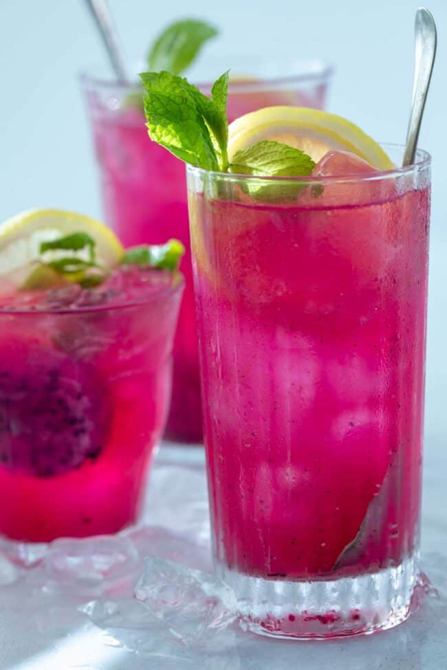 4 glasses filled with bright pink mango dragonfruit refresher. Lemon slices and mint leaves garnish the drinks.