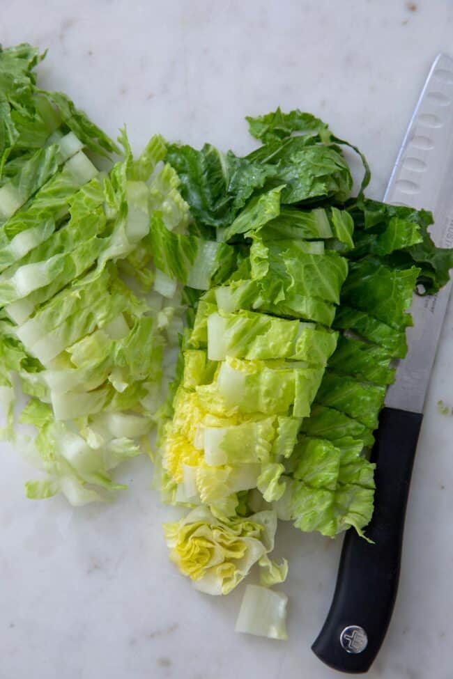 Chopped lettuce with a knife (with a black handle) sitting next to it.