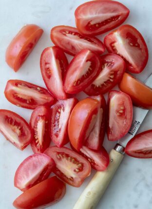 Roma tomatoes on a white cutting board cut in quarters lengthwise