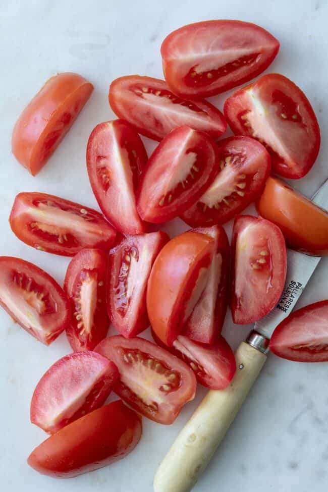 Roma tomatoes sliced in quarters on a white cutting board with a knife